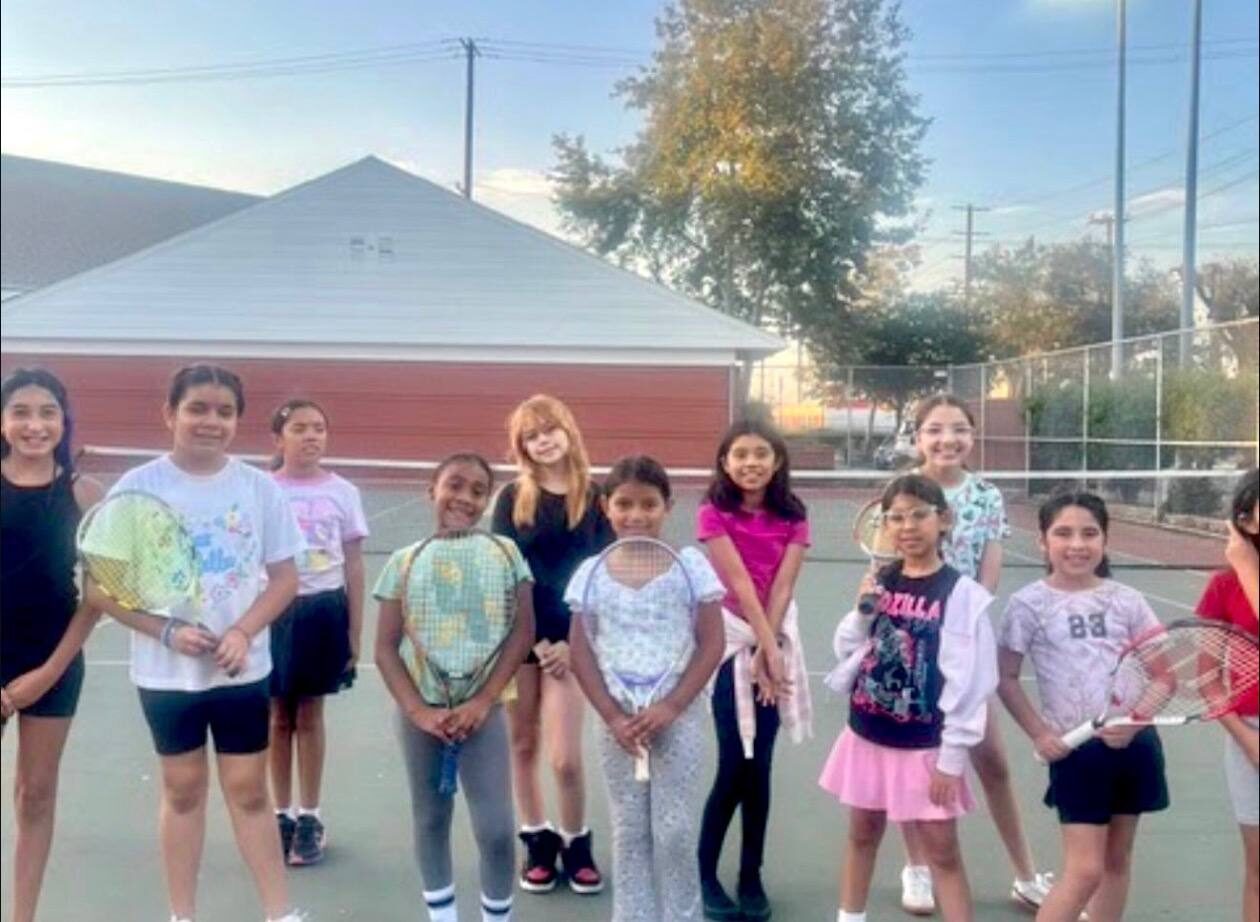 Ten girls on a tennis court at sunset holding the rackets they received from Second Serve