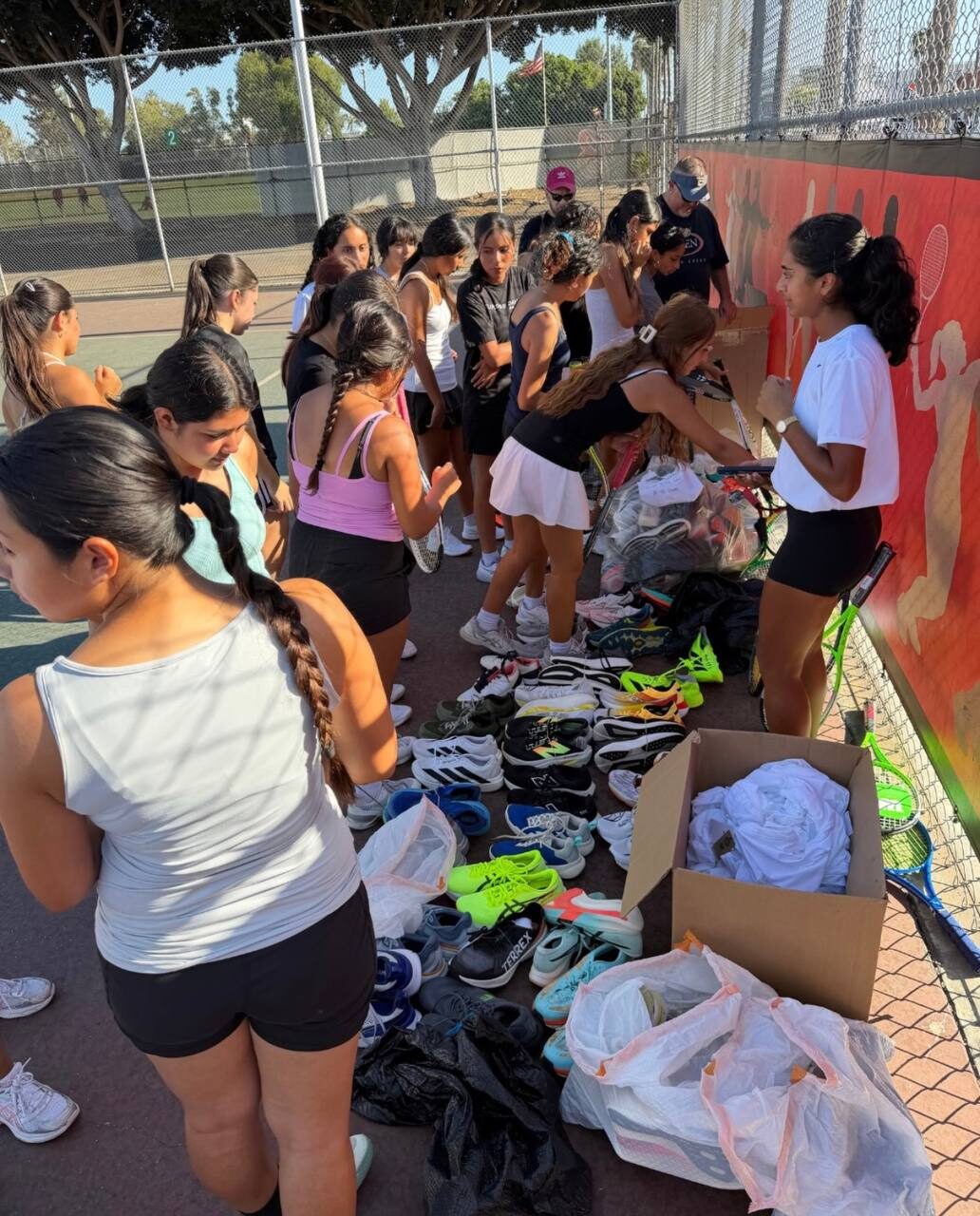 A high-school girls’ tennis team choosing shoes from boxes of donated equipment on the court